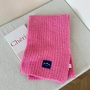 Detail of pink knitted scarf featuring thick plush texture and navy blue woven label