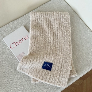 Close-up of beige soft thick scarf with a vintage blue woven label on a minimalist background