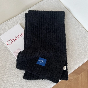 Close-up of thick black chenille knit scarf with blue logo label on soft fabric surface