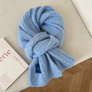 Close-up of sky blue fuzzy scarf texture with an elegant embroidered brand label