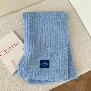 Detailed close-up of light blue chunky knit scarf with a woven brand logo label