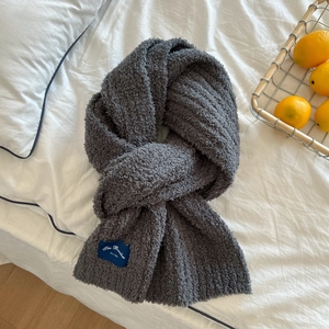 Detail of soft dark grey fleece scarf with blue brand label on white bedding background