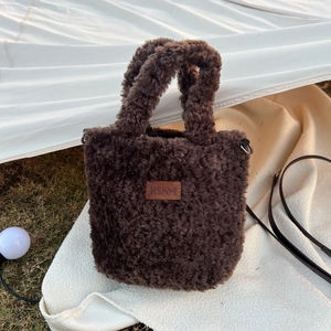 Detail of plush brown tote bag with leather logo patch on a cozy white outdoor blanket