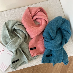 Flat lay of colorful 100% wool knitted scarves in green, pink, and blue with ribbed ends