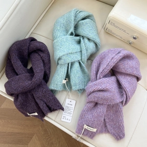 Chunky alpaca knit scarves in purple and mint green displayed on a soft leather bench
