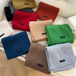 Detailed view of stacked knitted wool scarves in vibrant colors with 100 percent wool tags