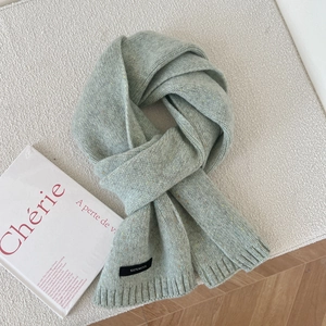 Detail of light green 100% wool knitted scarf showing texture and material label