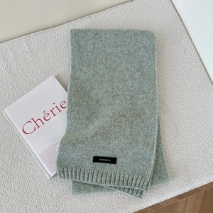 Detail view of light green knitted wool scarf with 100% WOOL tag and ribbed texture