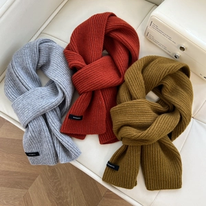 Close-up of 100% wool knit scarves in grey, orange, and yellow on a leather sofa