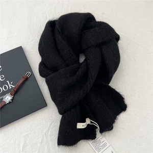 Close-up of black knitted alpaca scarf with white woven label and soft fluffy texture