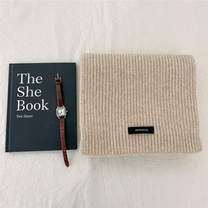 Close-up of beige rib-knit 100% wool scarf with material tag on textured fabric