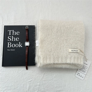Detail of cream alpaca wool knit scarf texture with luxury brand tags and watch decor