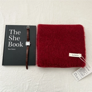Detail of deep red alpaca wool scarf with brand label and leather watch on tablecloth