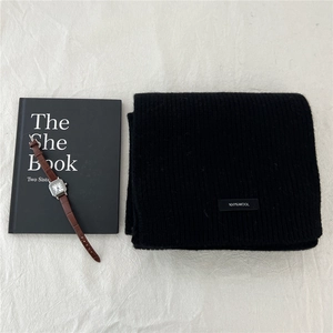 Detail of 100% wool knitted scarf with a black texture next to a classic watch