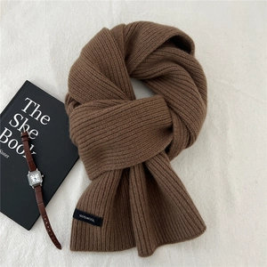 Detail of dark brown knitted wool scarf showing vertical rib texture and 100% wool label