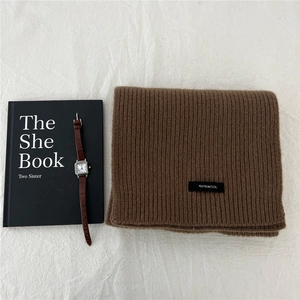 Detail of rib-knit wool scarf texture with 100% WOOL label and minimalist accessories