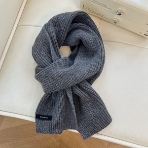 Detailed texture of thick dark grey wool scarf with 100% wool label on leather surface
