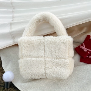 Close-up of white plush quilted handbag featuring thick faux fur handle for winter fashion