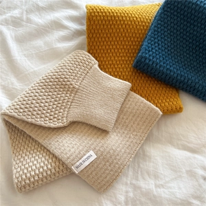 Macro shot of knitted neck warmers in beige, yellow, and blue with honeycomb texture