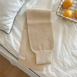 Detail of beige chunky knit scarf with waffle texture on white bedding with basket