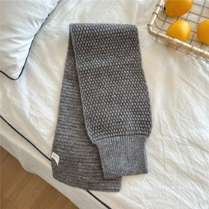 Detail of dark grey chunky knit scarf texture with a stitched label on a white surface