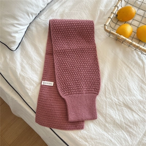 Detail of dusty pink chunky knit scarf with ribbed texture and brand label on white linen