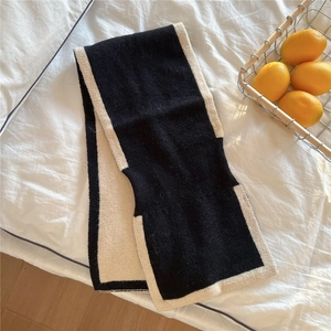 Détail d'une écharpe en maille noire avec bordure contrastée crème sur fond blanc