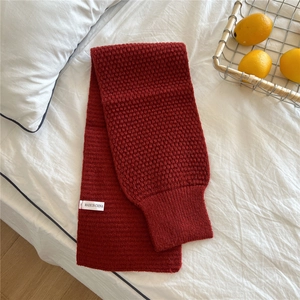 Detail of burgundy knit scarf showing thick ribbed texture and brand label on bed
