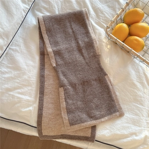 Détail d'une écharpe en maille bicolore marron et beige sur un décor de lit blanc