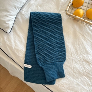 Close-up of dark blue knit scarf showing textured pineapple stitch and white brand label