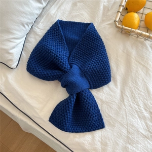 Detail of navy blue chunky knit scarf with cross-over pull-through slot on white bedding