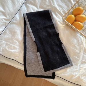 Détail d'une écharpe en maille bicolore noir et gris posée sur un lit blanc douillet