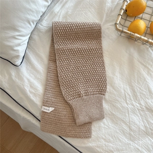 Macro detail of beige knit scarf with honeycomb texture and woven label on white bedding