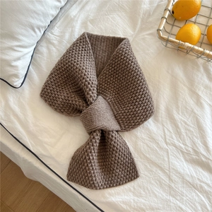 Detail of coffee knit scarf with waffle texture and cross-over closure on white bedding