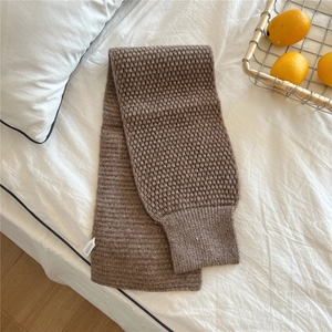 Close-up of brown chunky knit scarf with wave texture and rib-knit edge on bed