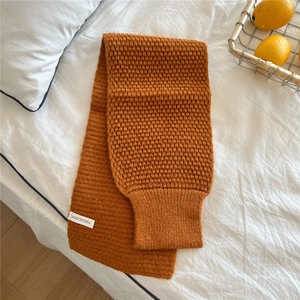 Close-up detail of caramel knitted scarf texture with waffle pattern on white bedding