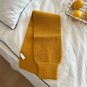 Close-up of ginger yellow knitted scarf with textured wave pattern and brand wash label