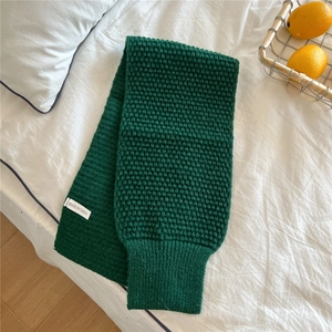 Detail of dark green chunky knit scarf featuring honeycomb texture and white origin label
