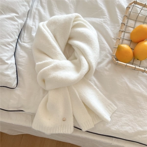 Detail of soft ivory knitted scarf featuring a decorative gold button and ribbed texture