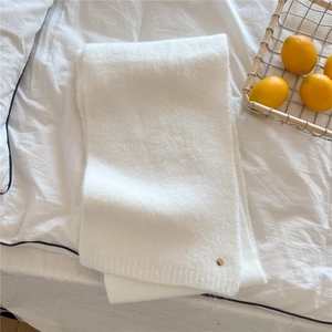 Close-up of soft white knit scarf with rib edges and a round gold metal logo tag