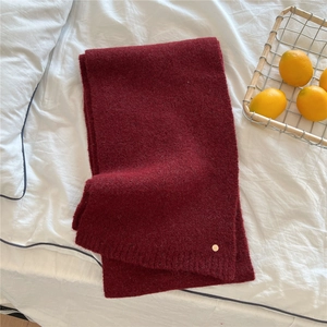 Close-up of deep red knitted winter scarf with thick wool texture and gold logo detail