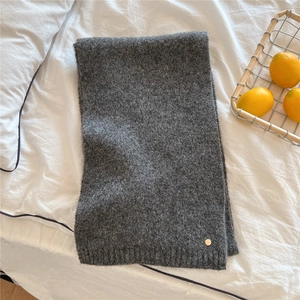 Detailed close-up of dark grey knitted scarf with round gold logo tag on soft fabric