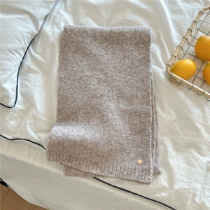Detail of oat-colored knitted long scarf with golden charm on white bedding decor