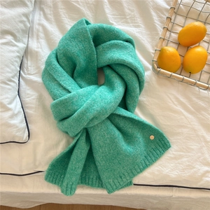 Close-up of mint green chunky knit scarf featuring a decorative gold metal buckle accent