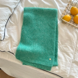 Detail of mint green knitted scarf texture with small gold metal logo on white bedding