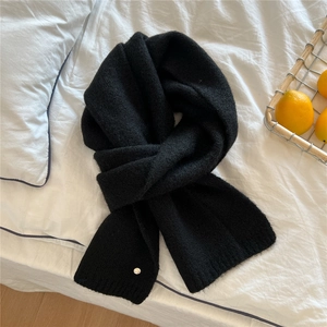 Detailed knit texture of a black winter scarf with a small metal charm on white bedding