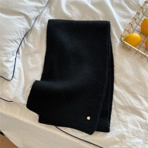 Detail of black knit scarf featuring a soft texture and elegant gold round metal charm