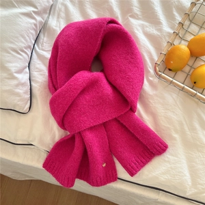Detail of rose red knit scarf with ribbed edges and small round golden logo tag