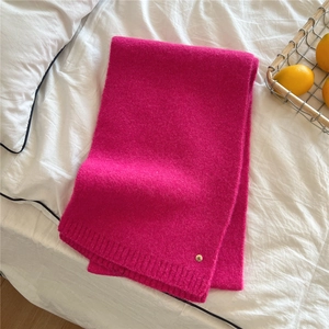 Detailed texture of fuchsia knit scarf with ribbed edges and a round gold metal logo