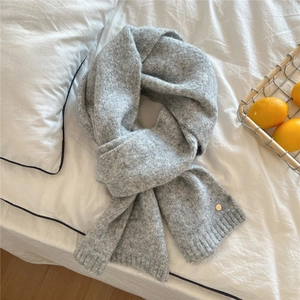 Detail of grey knitted winter scarf featuring ribbed edges and a small metal logo tag